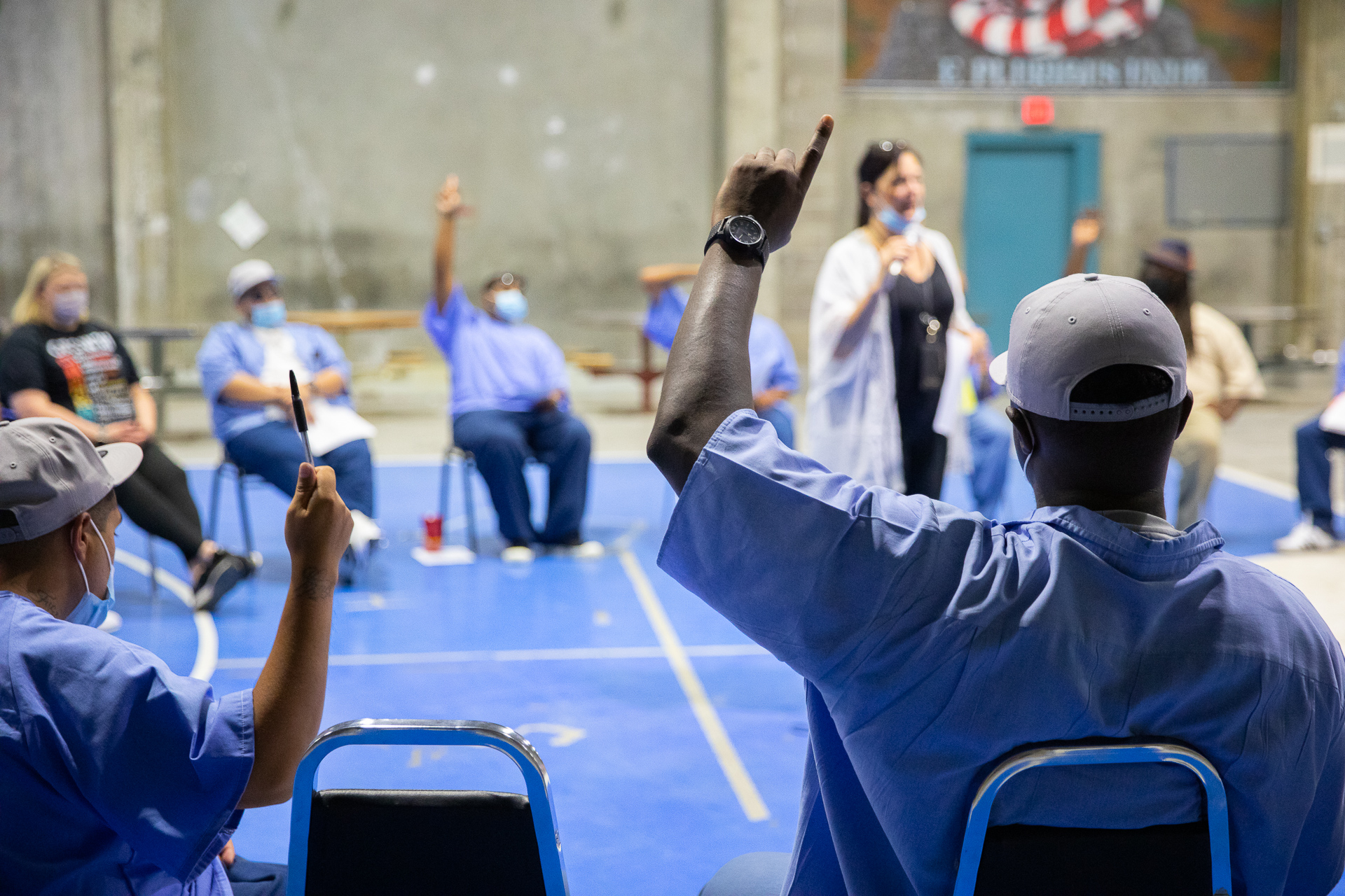 Folsom Prison inmates and participants in the restorative justice program sit in a circle of chairs inside the facility's gym wearing blue prison garb, some with their fingers in the air in response to a speaker from Sac State's group.