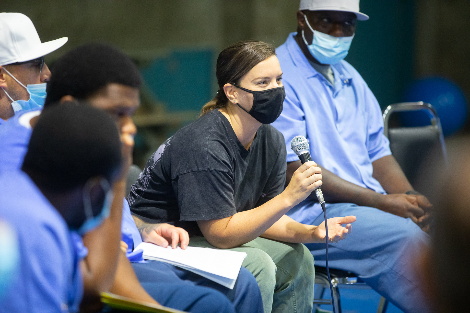 Dressed in a black top and green bottoms, a graduate student in Social Work who is part of the restorative justice group speaks to inmates via microphone during a workshop session at Folsom Prison.