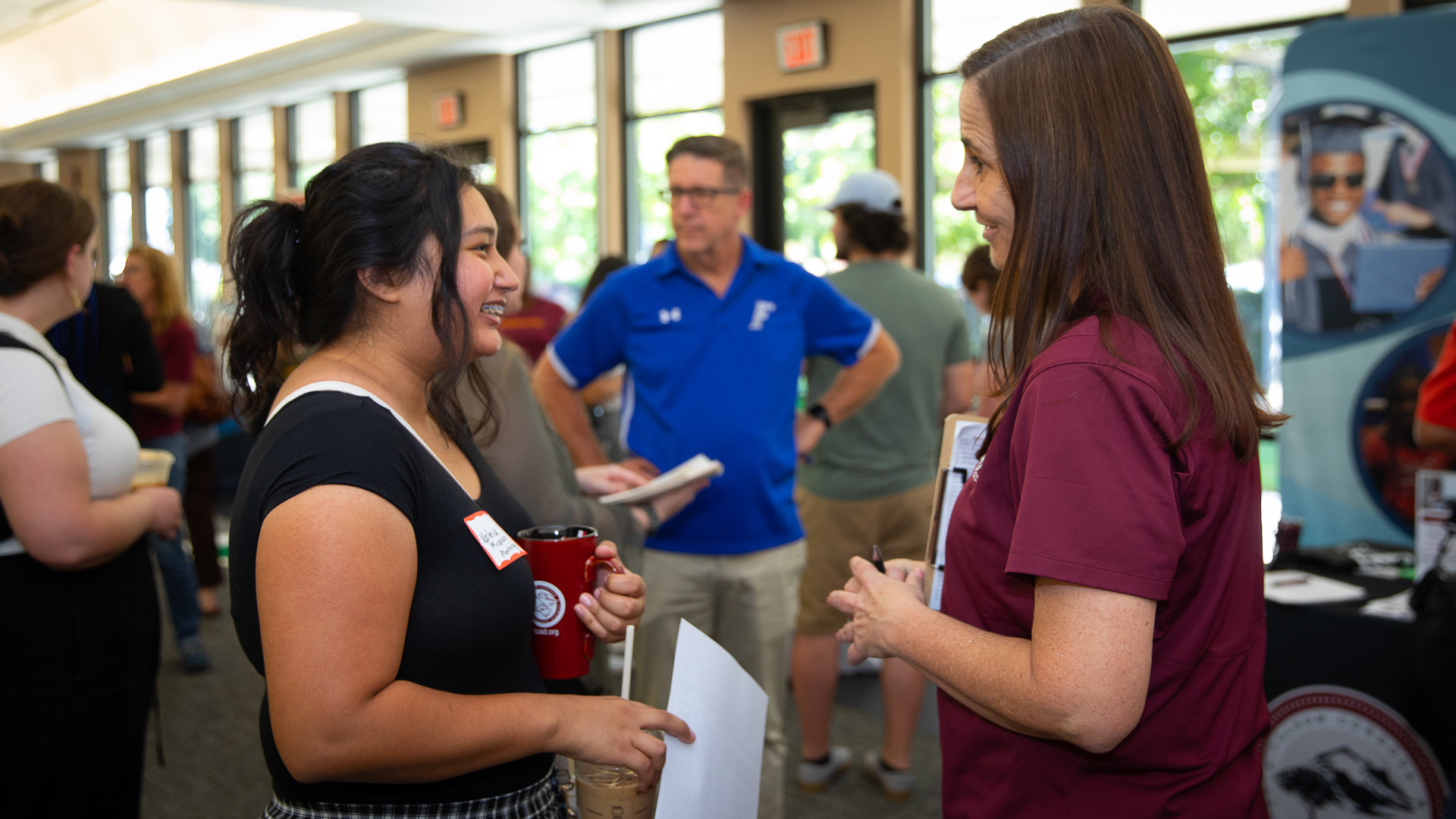 Recent Sac State graduate Valeria Miranda, wearing a black shirt and smiling, speaks to a representative of Folsom-Cordova Unified School District, who is dressed in a burgundy T-shirt.