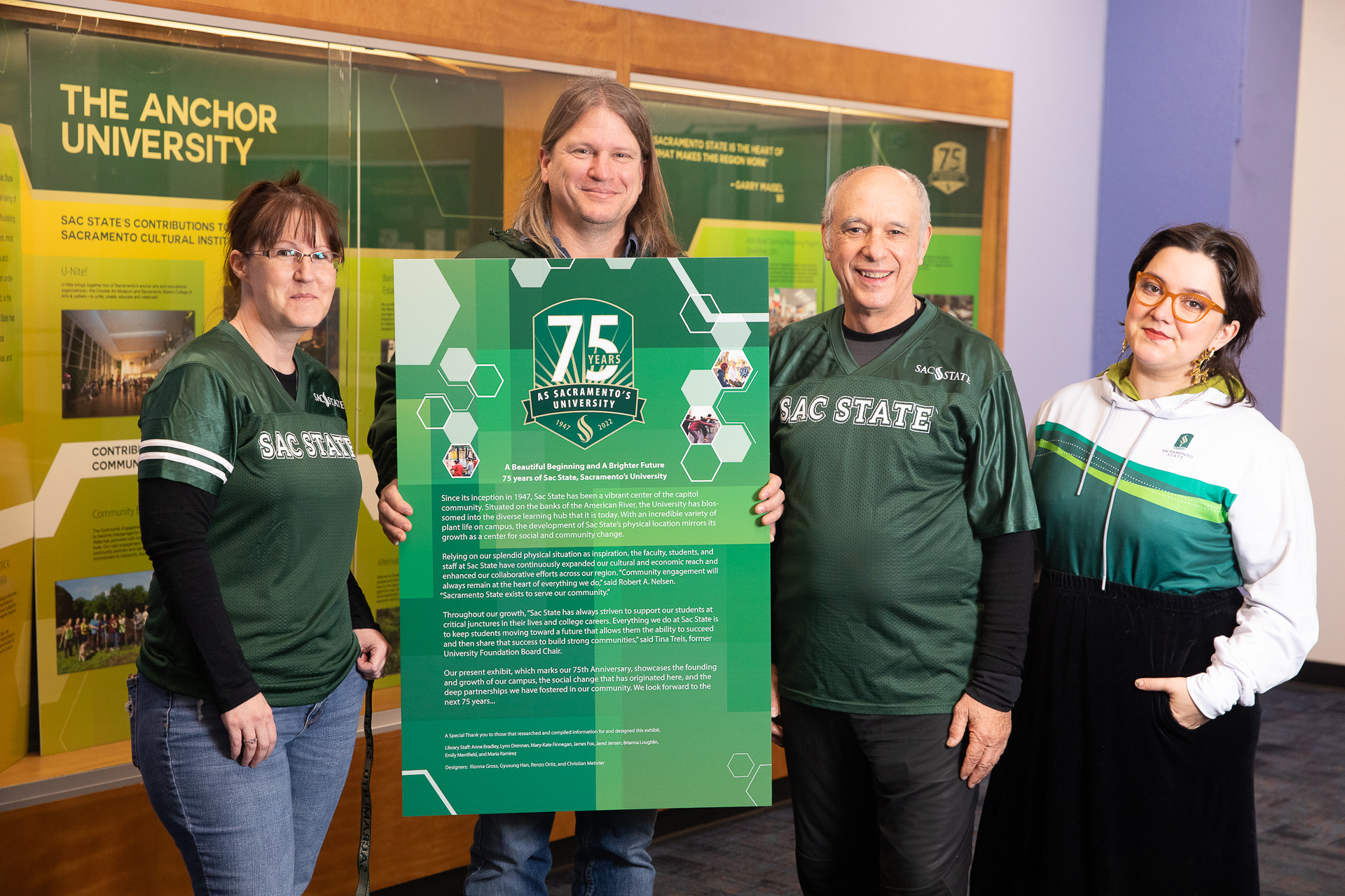 Members of the University Library and Archives staff pose in front of the Sacramento State 75th Anniversary exhibit display.