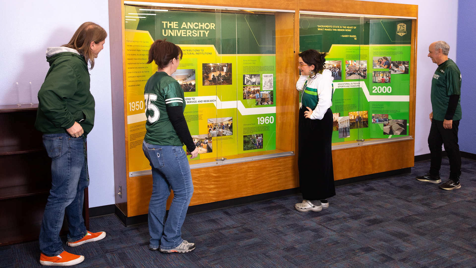 Members of the University Library and Archives staff observe the Sacramento State 75th Anniversary exhibit display put together by their team.