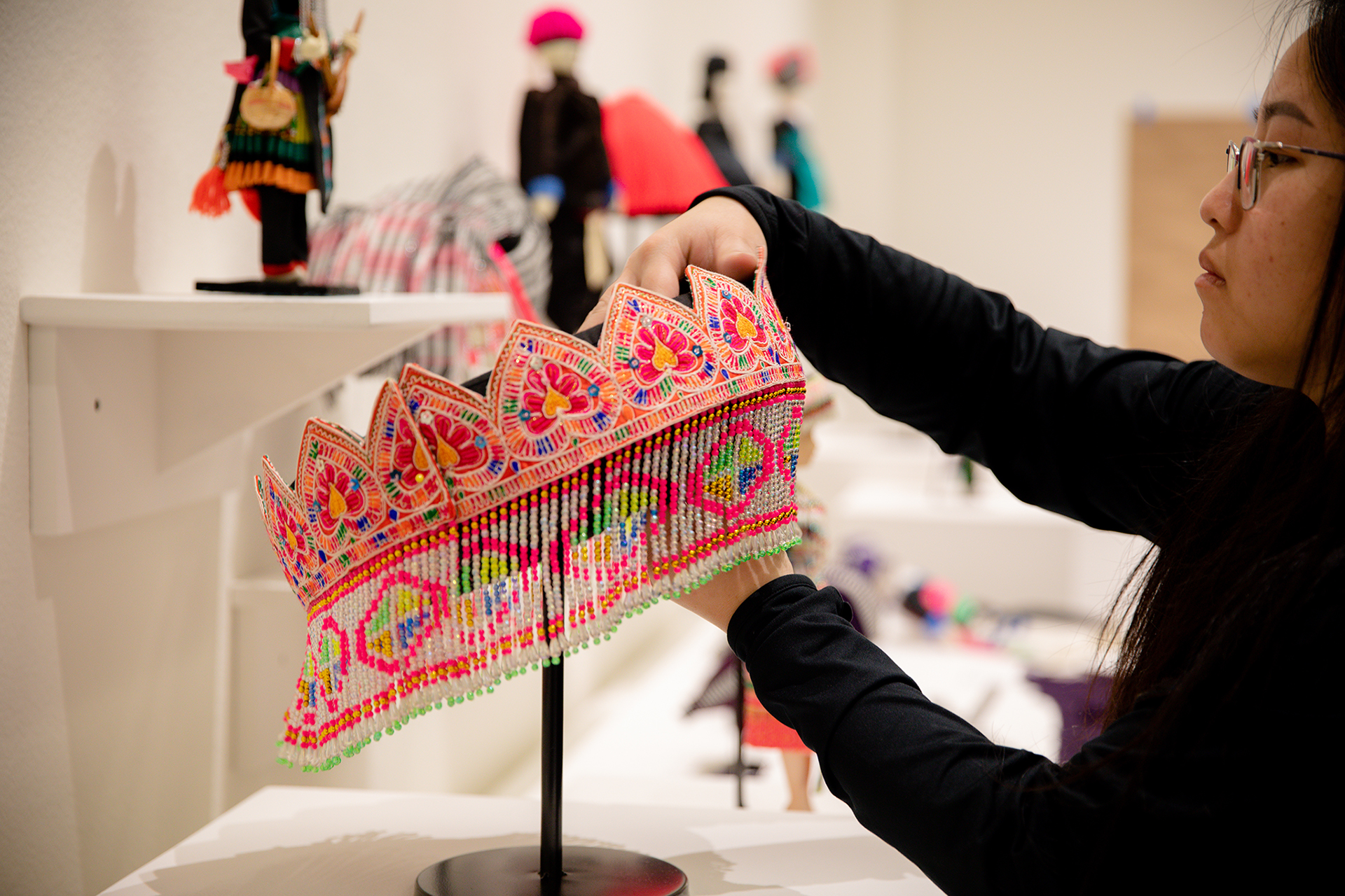 A woman adjusts a Hmong headpiece, decorated in orange, pink, blue, green and other beads, on display as part of an exhibit at Sac State.
