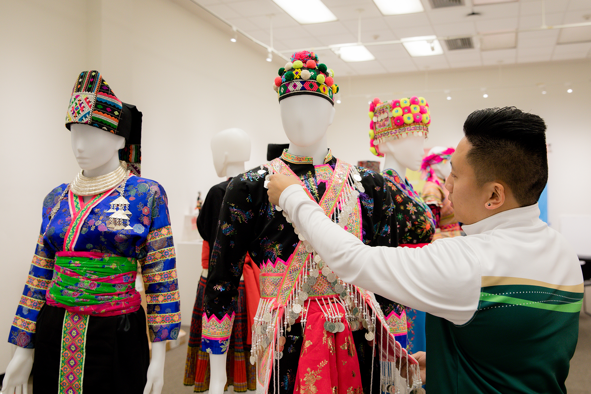 A member of the group who put together a Hmong cloth exhibit at Sacramento State adjusts one of the clothing items.