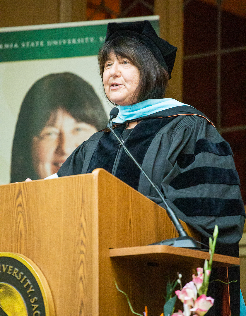 Wang Family Excellence Award recipient Joy Stewart-James, dressed in a graduation gown, stands at a podium, speaking at a recent commencement.