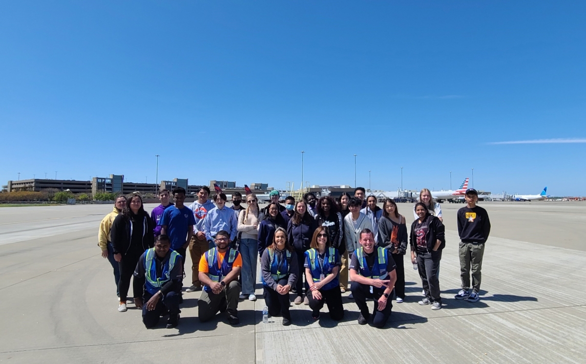 Participants of a youth leadership program pose together on the runway at an airport.