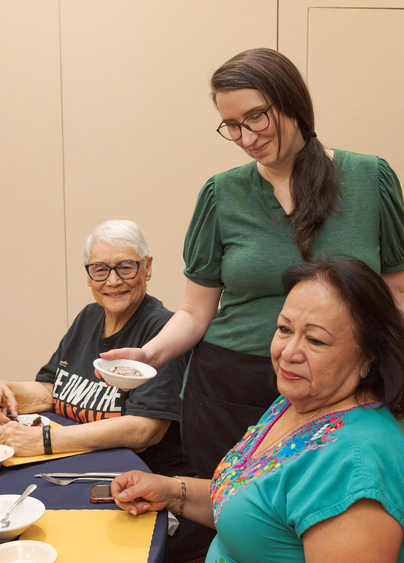 A volunteer at a senior center serves a meal to couple.