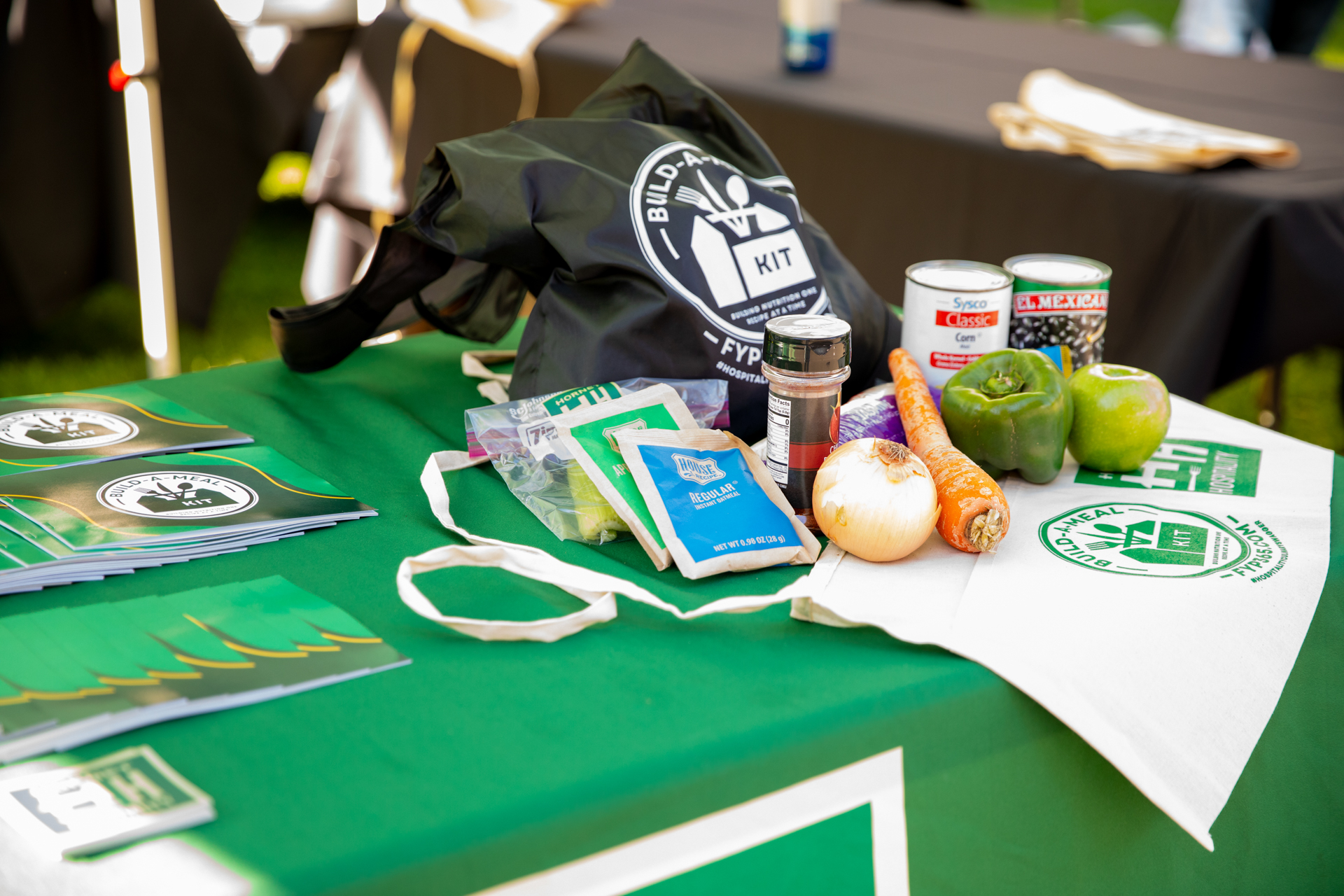 A bag, food items, and brochures sit on a table with a green tablecloth.