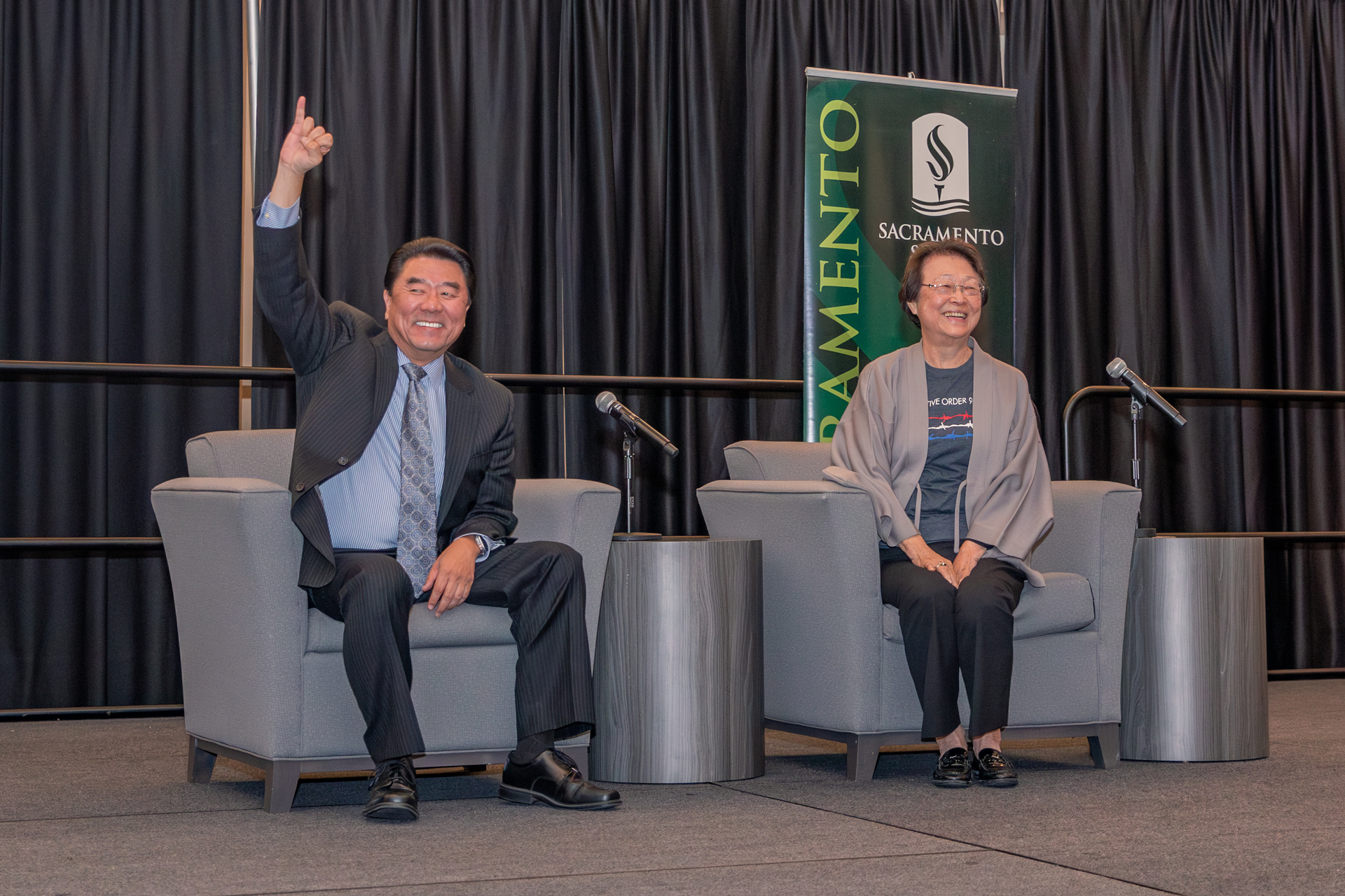 Two speakers pose on stage, one saluting Stingers Up, at a recent One Book Program event.