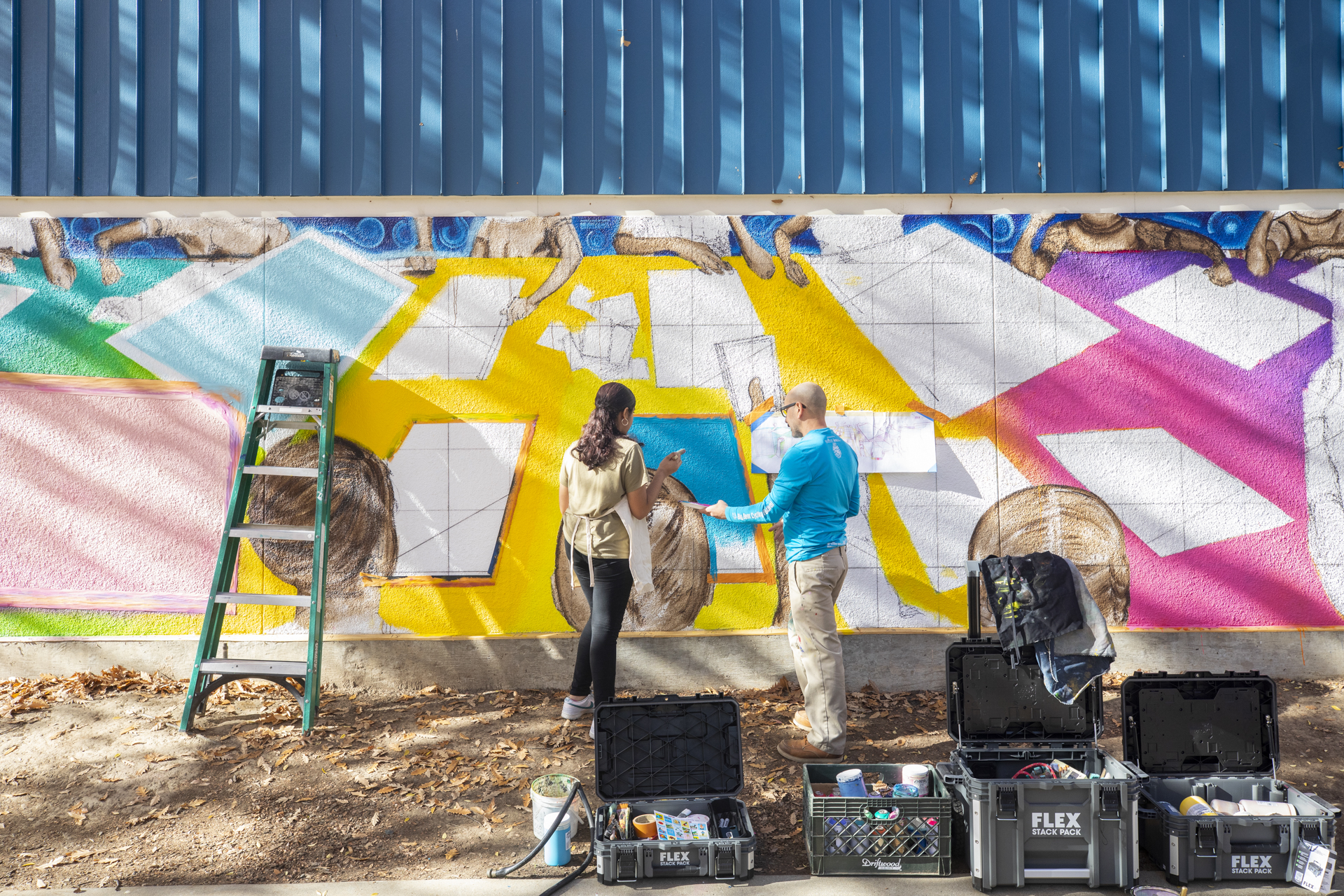 Washington Elementary student Hibba Zahid and Sac State professor Luis Garcia painting a mural, outdoors.