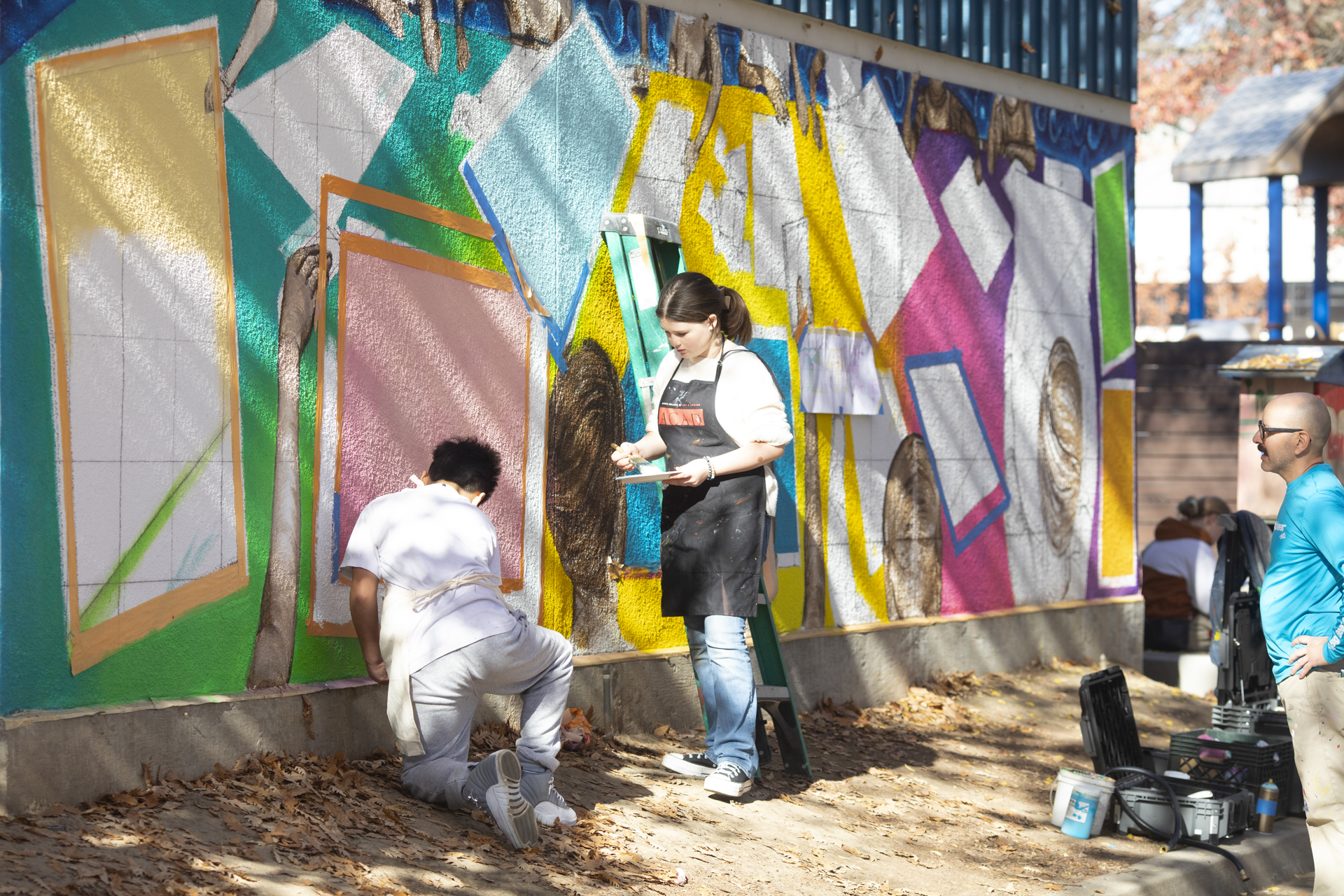 Two Washington Elementary students paint an outdoor mural as Sac State professor Luis Garcia watches.