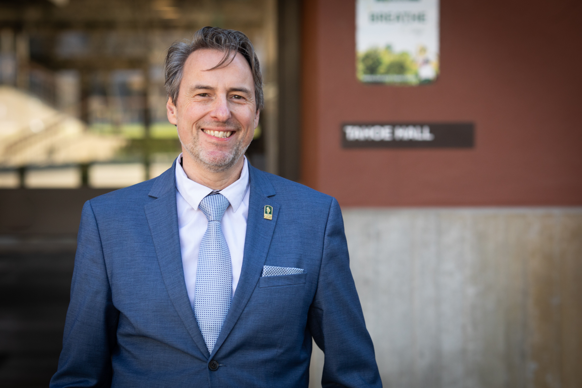 Sac State's new College of Business dean wearing a suit and tie poses at Tahoe Hall on campus while smiling. 