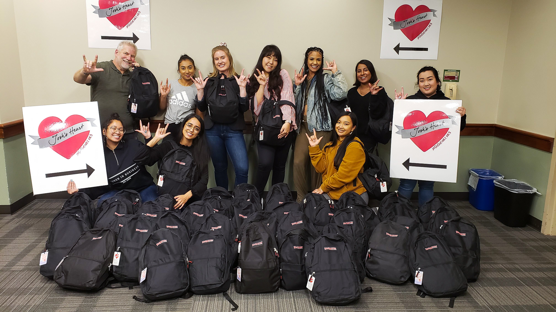 Josh's Heart volunteers pose with backpacks and signs with the organization's logo.