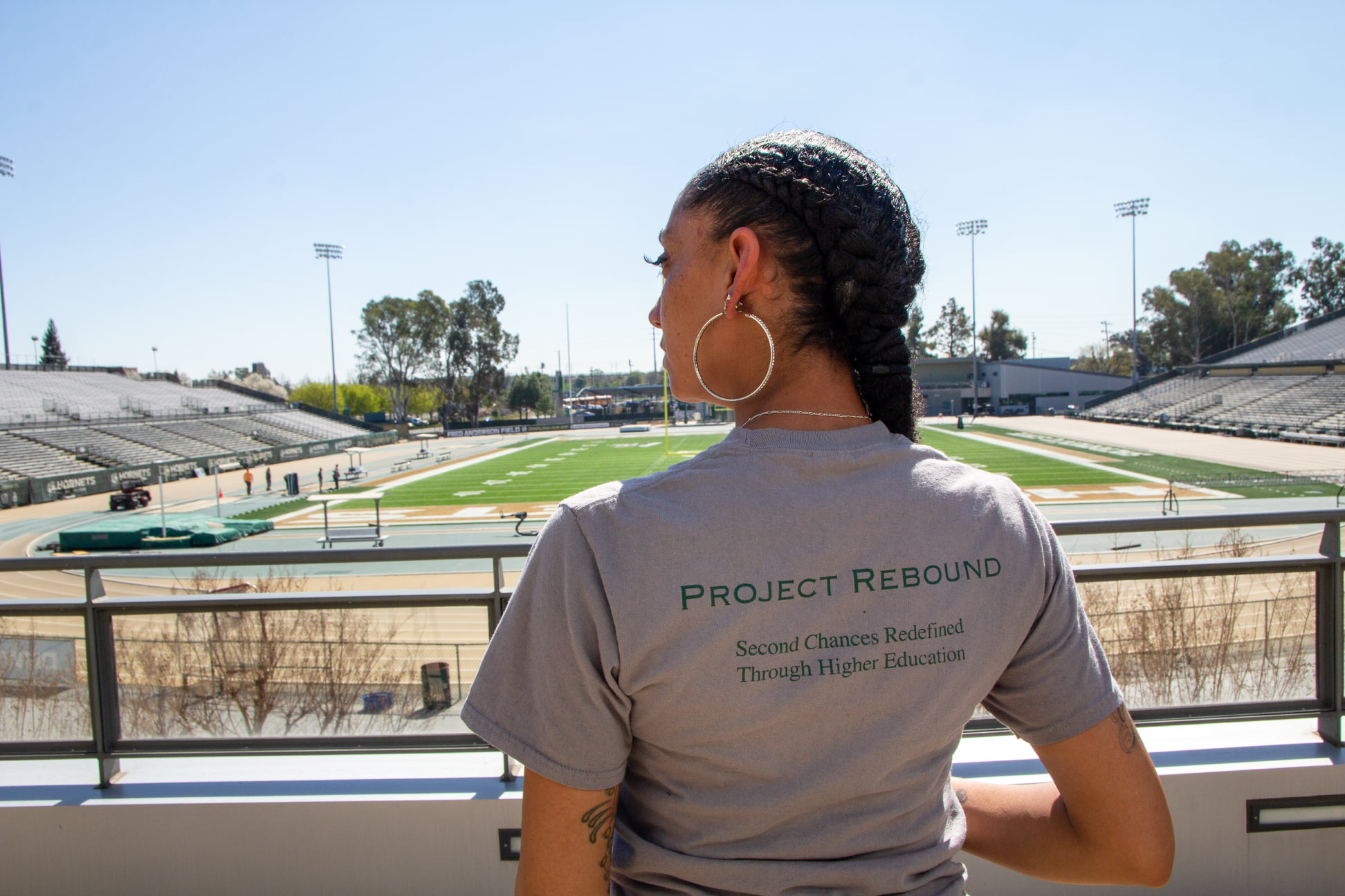 A woman in a t-shirt reading "Project Rebound" stands facing Hornet Stadium
