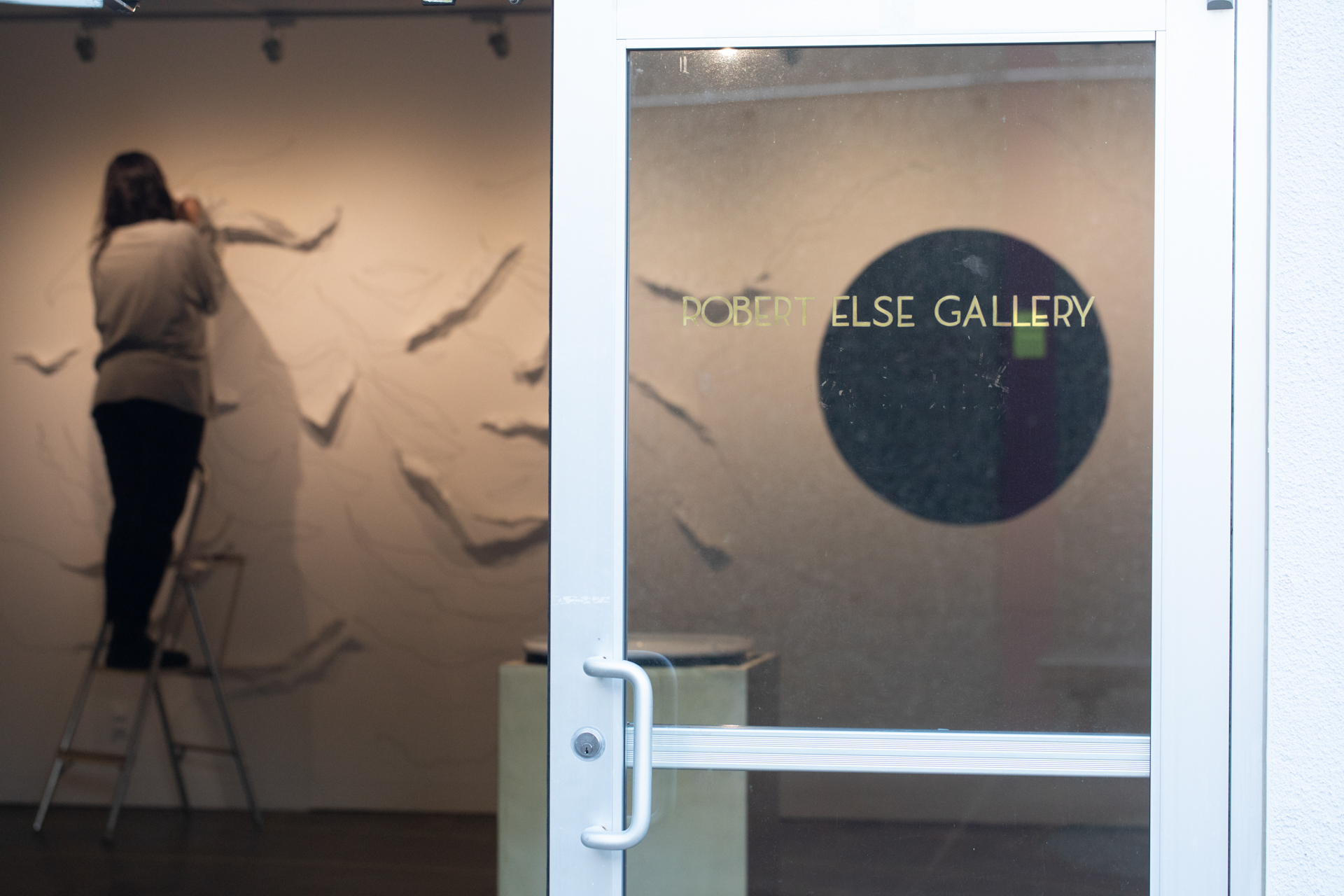 An artist standing on a step stool adjusts her display inside the Robert Else Gallery at Sac State.