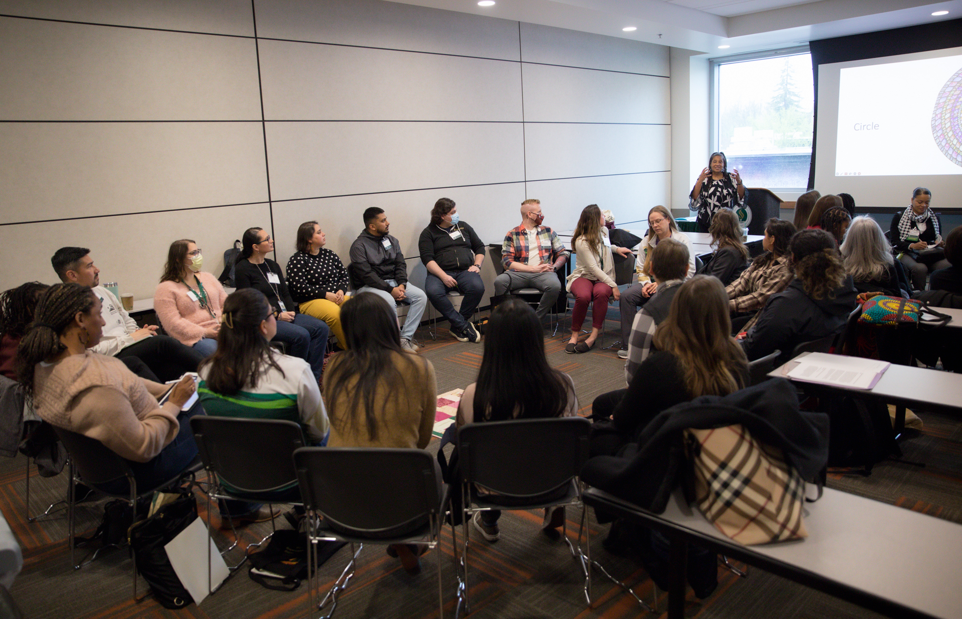 Symposium attendees participate in a workshop, sitting in a circle of chairs.