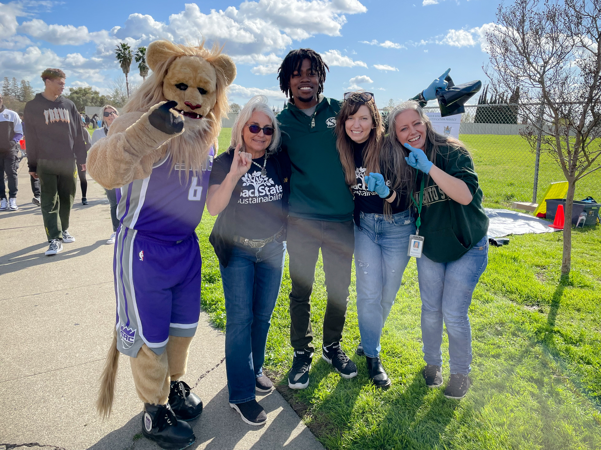 Four individuals pose, outdoors, with the Sacramento Kings mascot Slamson, making the "stingers up" hand gesture