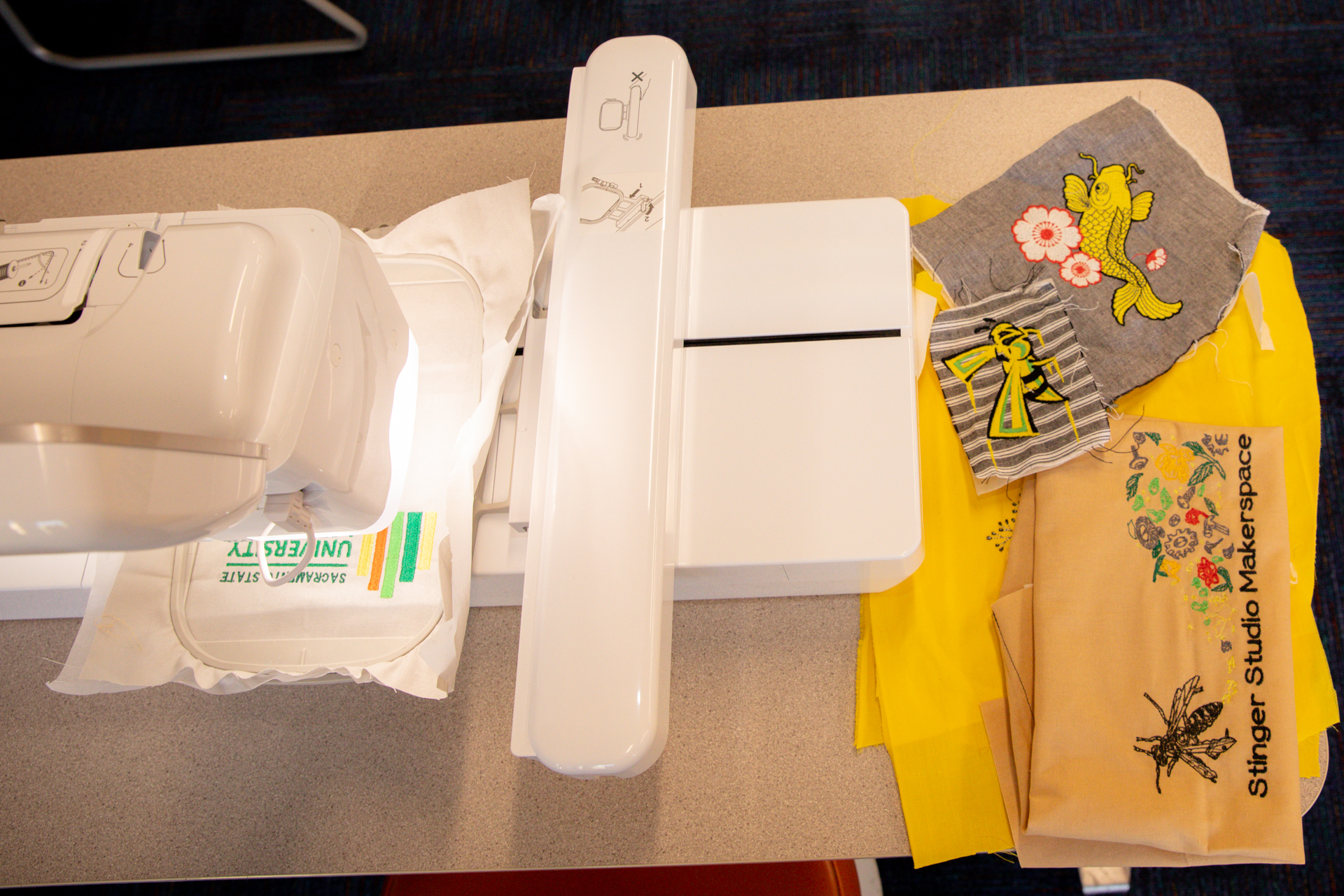 Various sewn items sit near a sewing machine at StingerStudio, including fabric with a University Library logo, Sac State Hornet logo and more.
