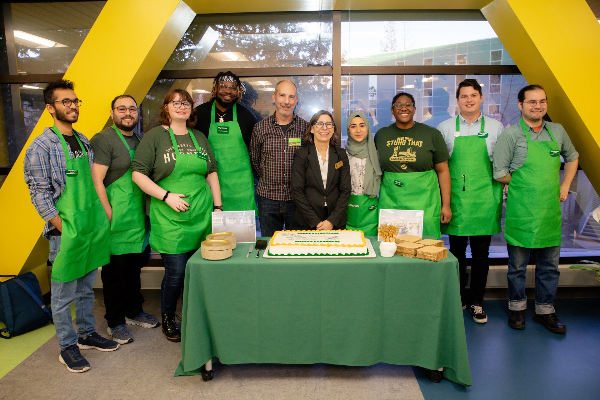 Makerspace and University Library staff stand behind a table with a celebratory cake during StingerStudio's grand opening.
