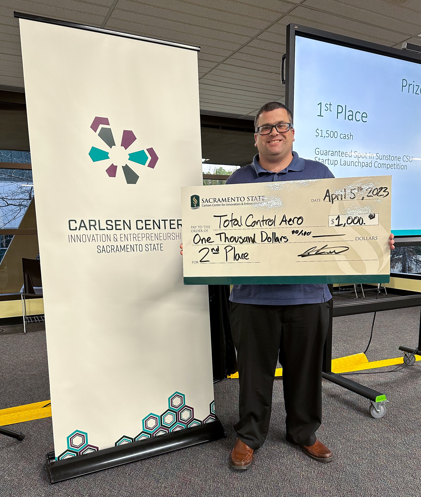The second-prize winner of a recent pitch competition holds an oversized version of the check he won.