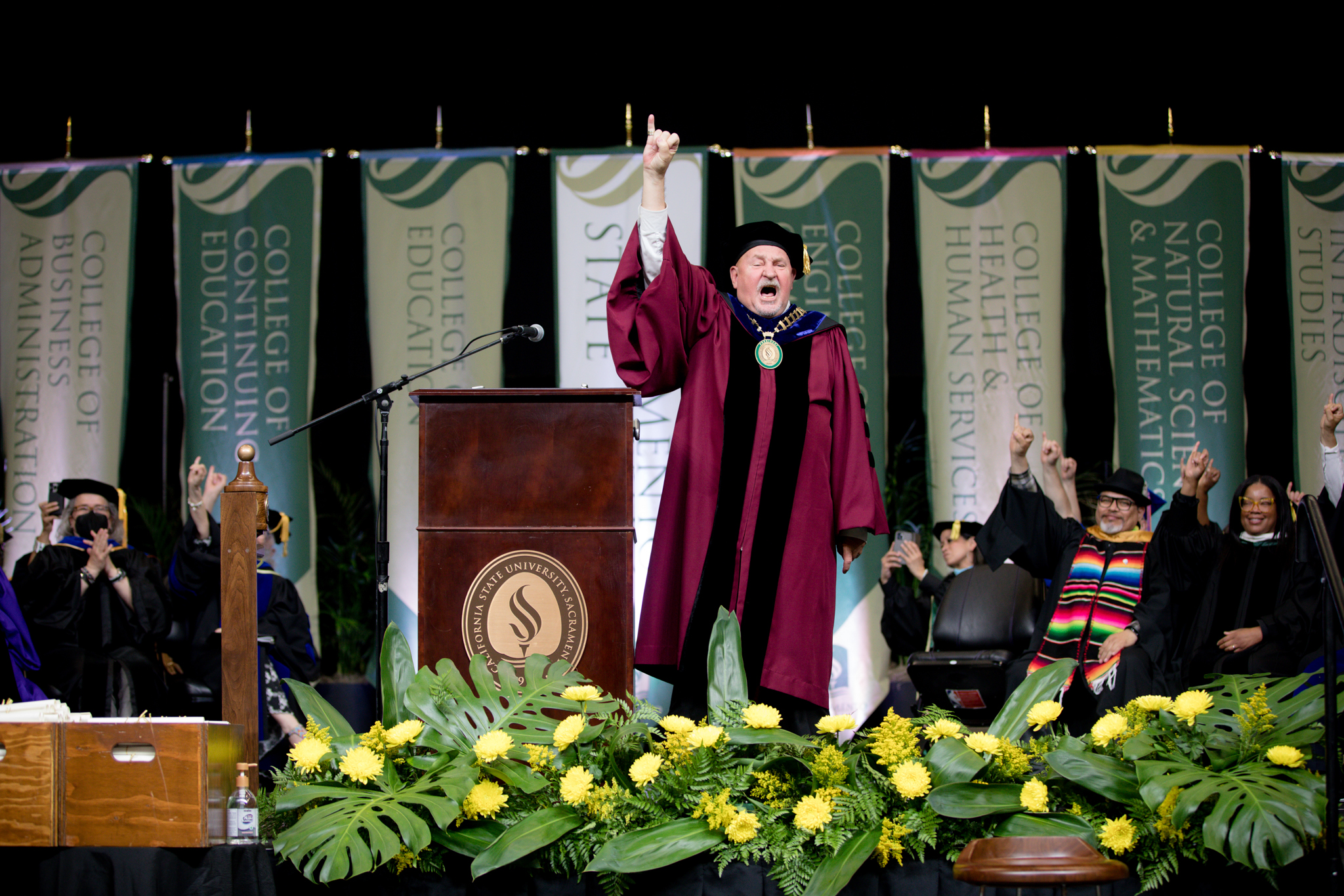 President Robert S. Nelsen, standing on the Commencement stage, giving the "Stingers Up" signal