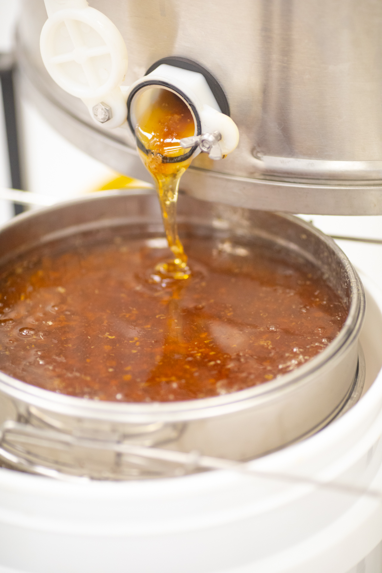 Honey flowing from a large metal vat into a pan.