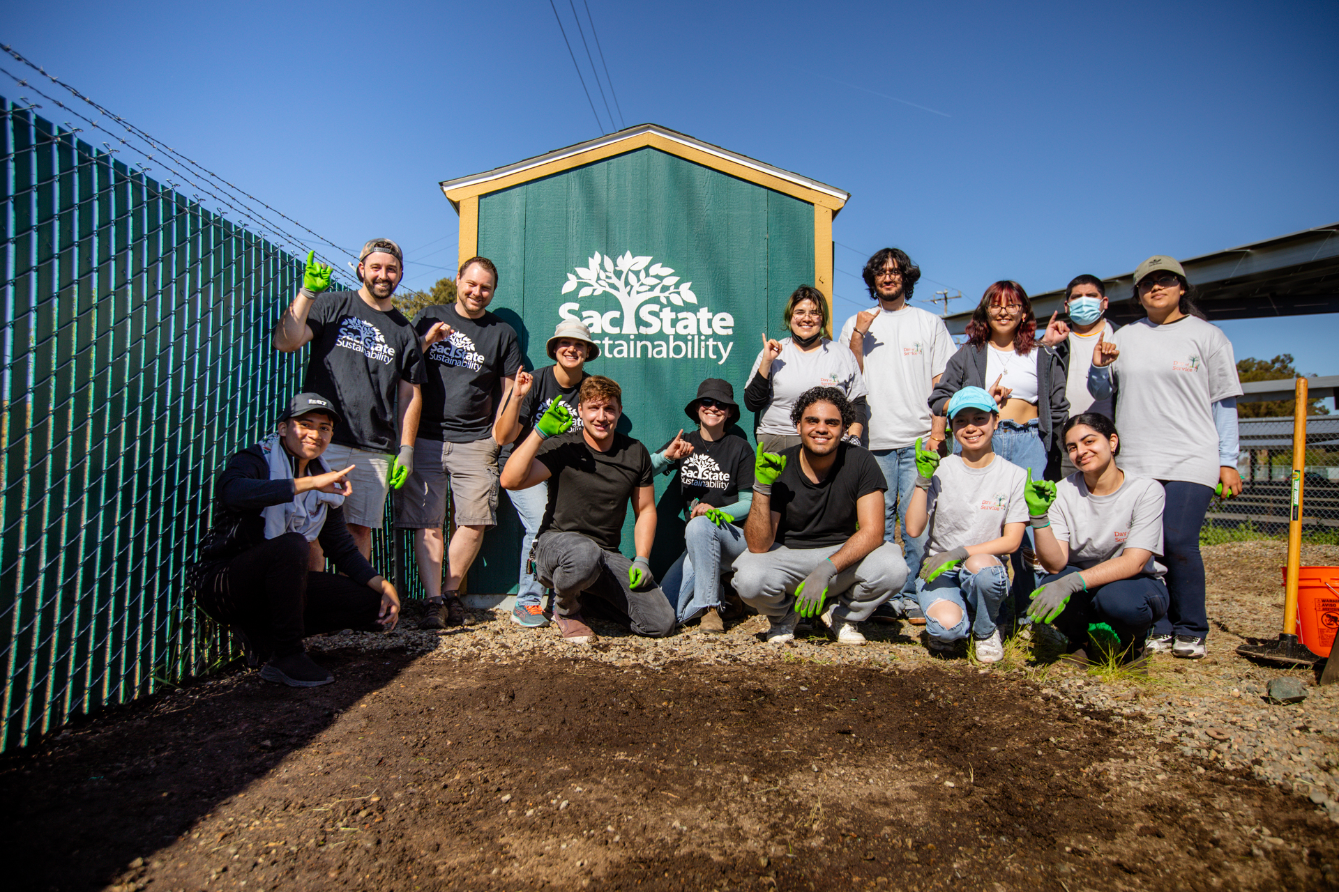Alternative Spring Break volunteers salute Stingers Up near a Sac State Sustainability shed.