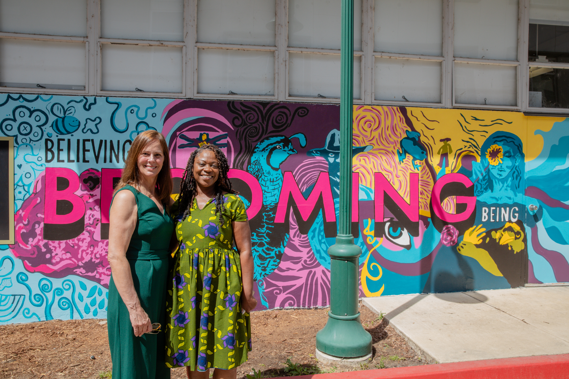 Campus staff pose in front of one of the Becoming murals.