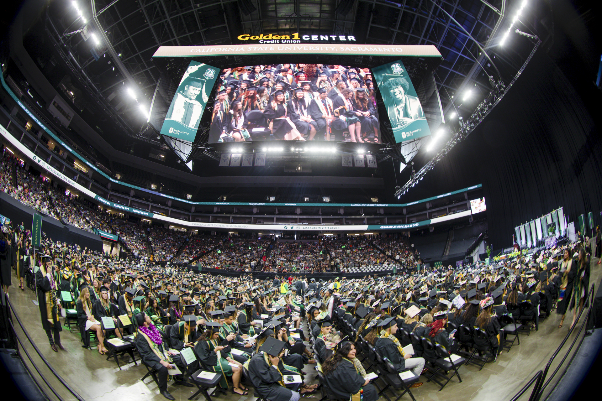 Graduates gathered on the floor of the Golden 1 Center, with the video display above and the audience in the background.