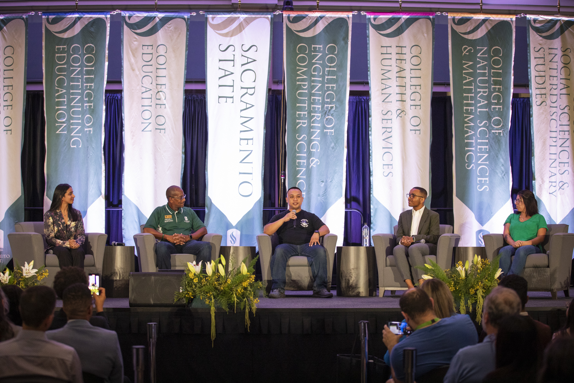 Five students seated on a stage in the University Union Ballroom, with banners behind them.