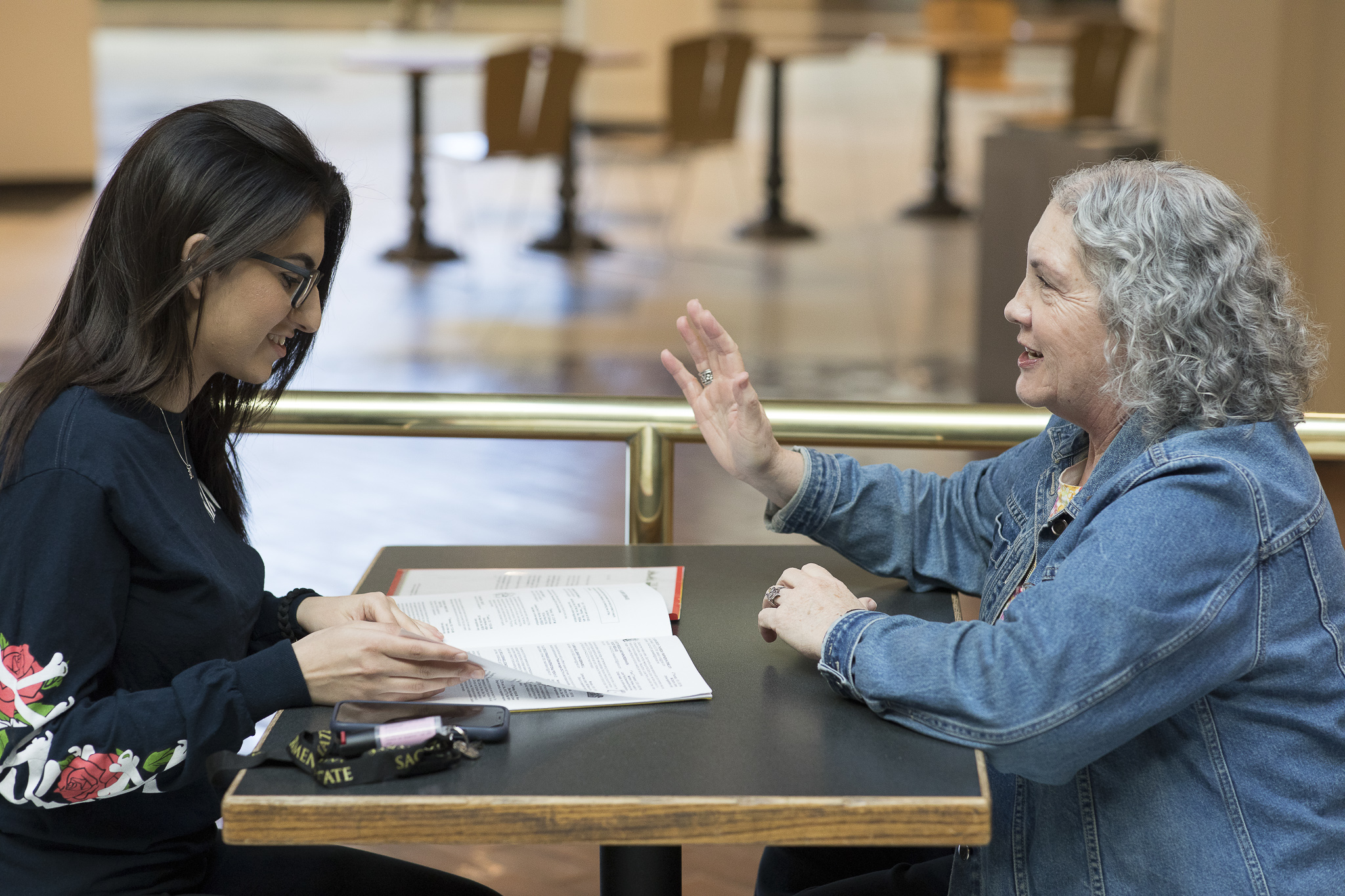 A young woman sits across from a table talking with an older woman.
