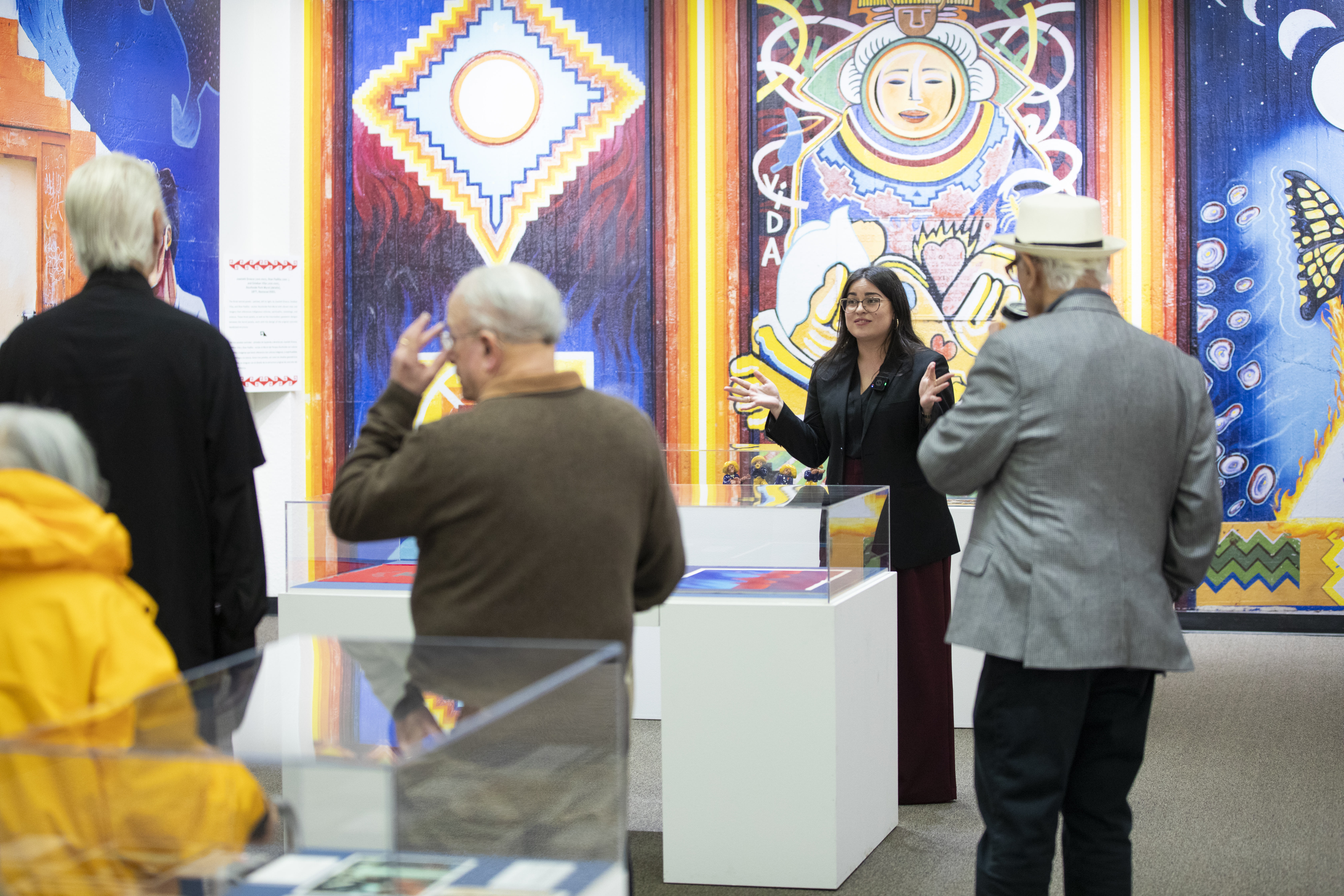 A woman discusses art on display to a crowd of people.