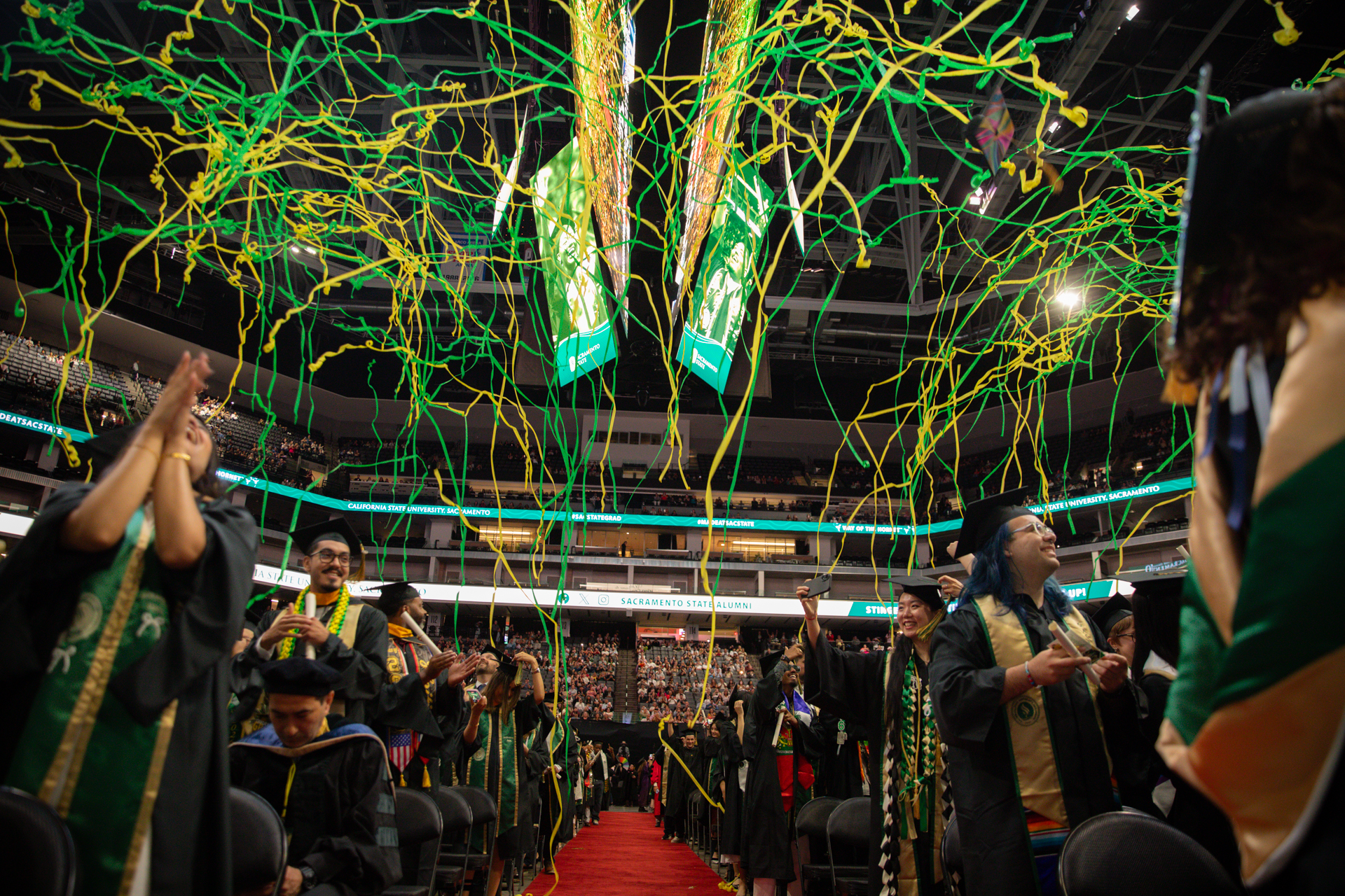 Green and gold streamers fall onto graduates in caps and gowns at arena during Commencement ceremony