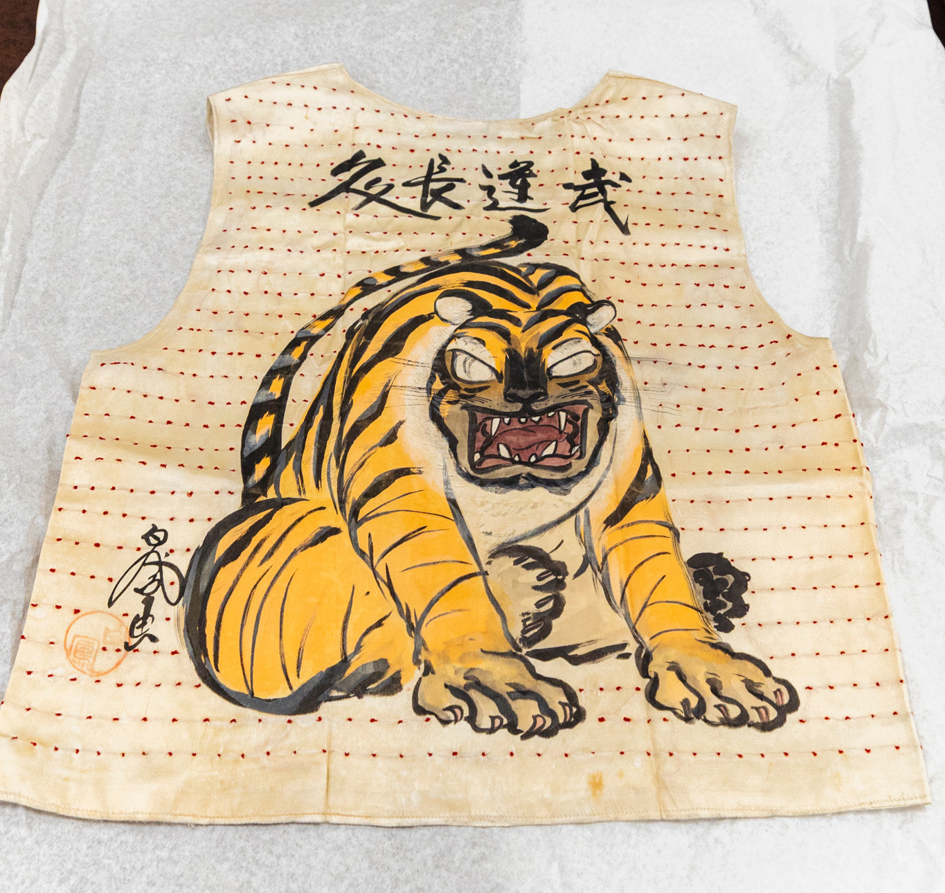White vest decorated with large painted tiger and small red knots.