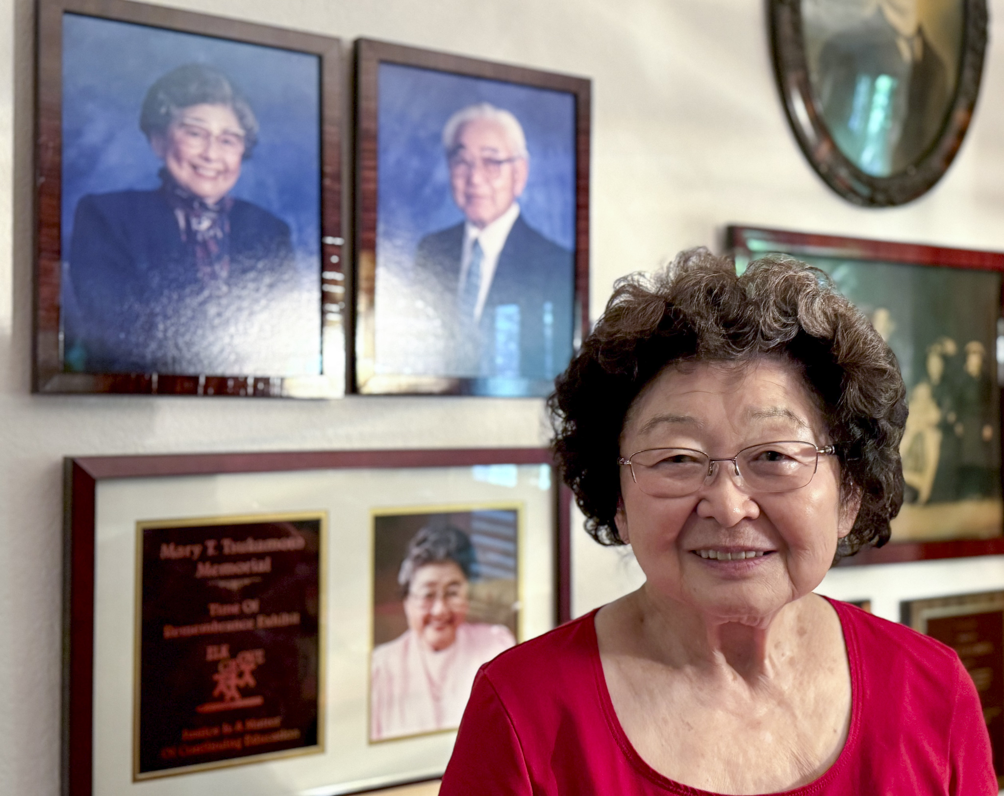 Mary Tsukamoto poses in front of framed photos of her parents, Mary and Alfred Tsukamoto.