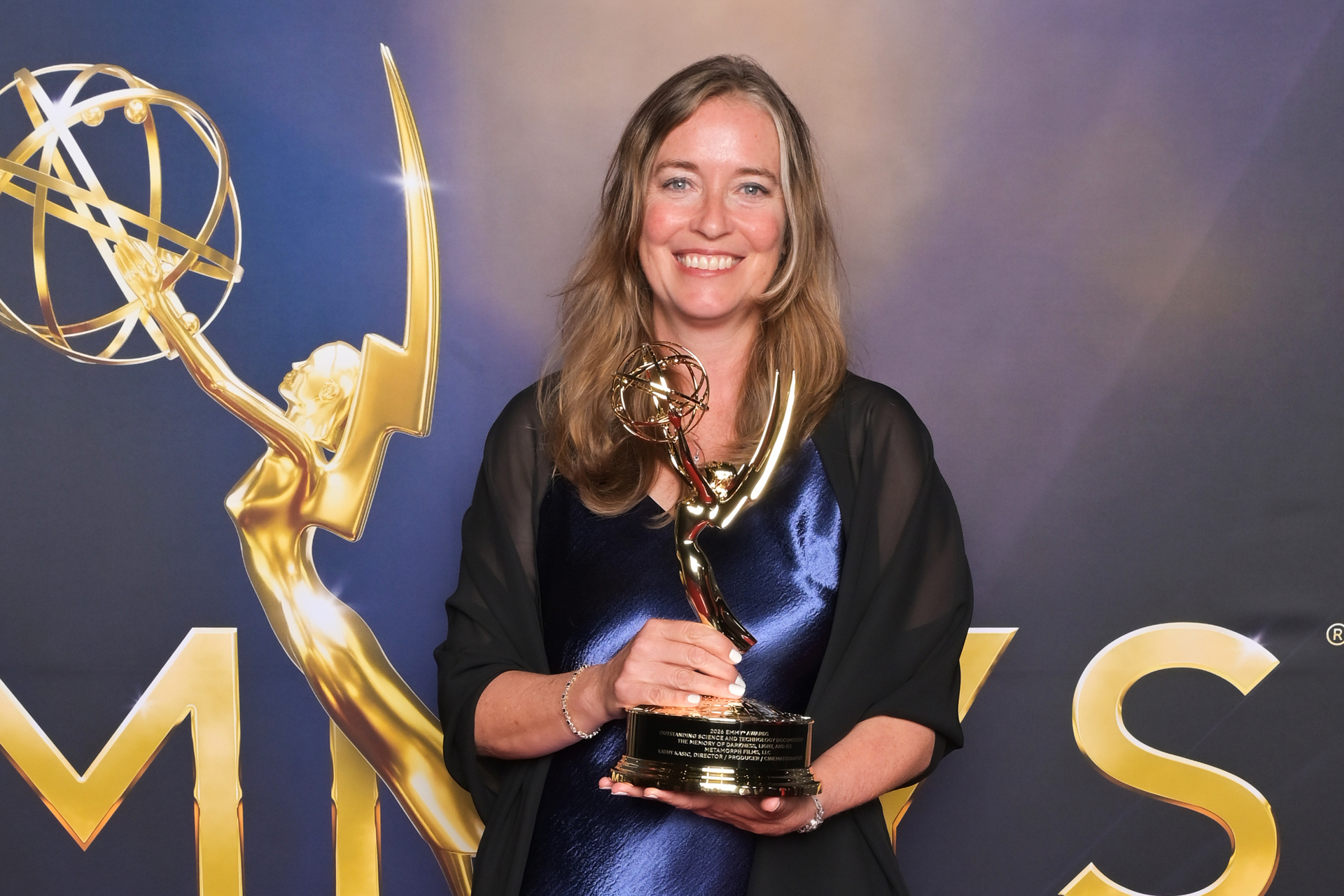Sacramento State profess Kathy Kasic wearing a purple dress and holding Emmy Award