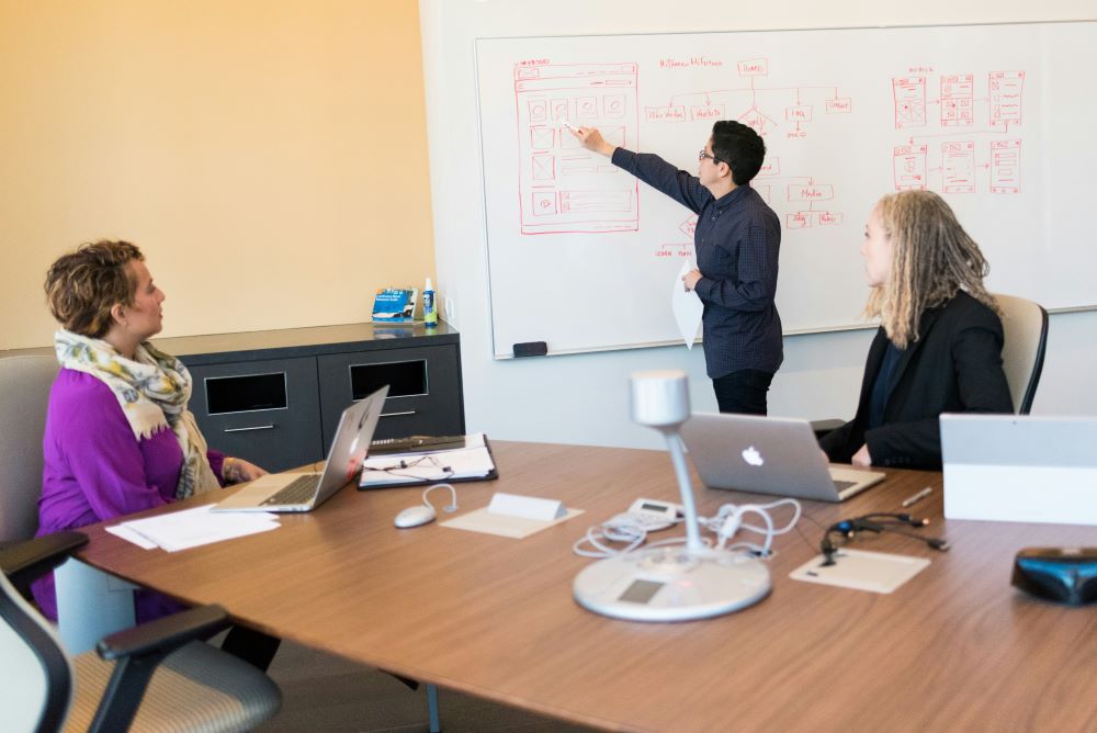 Person writing on whiteboard while two colleagues listen intently