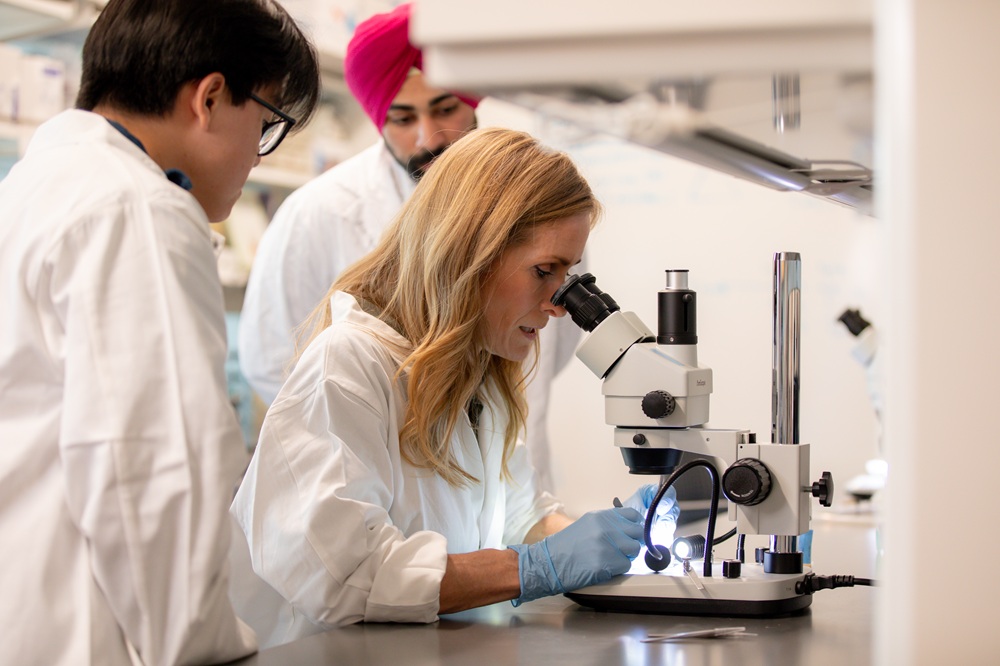 students and professor in lab coats looking through microscope