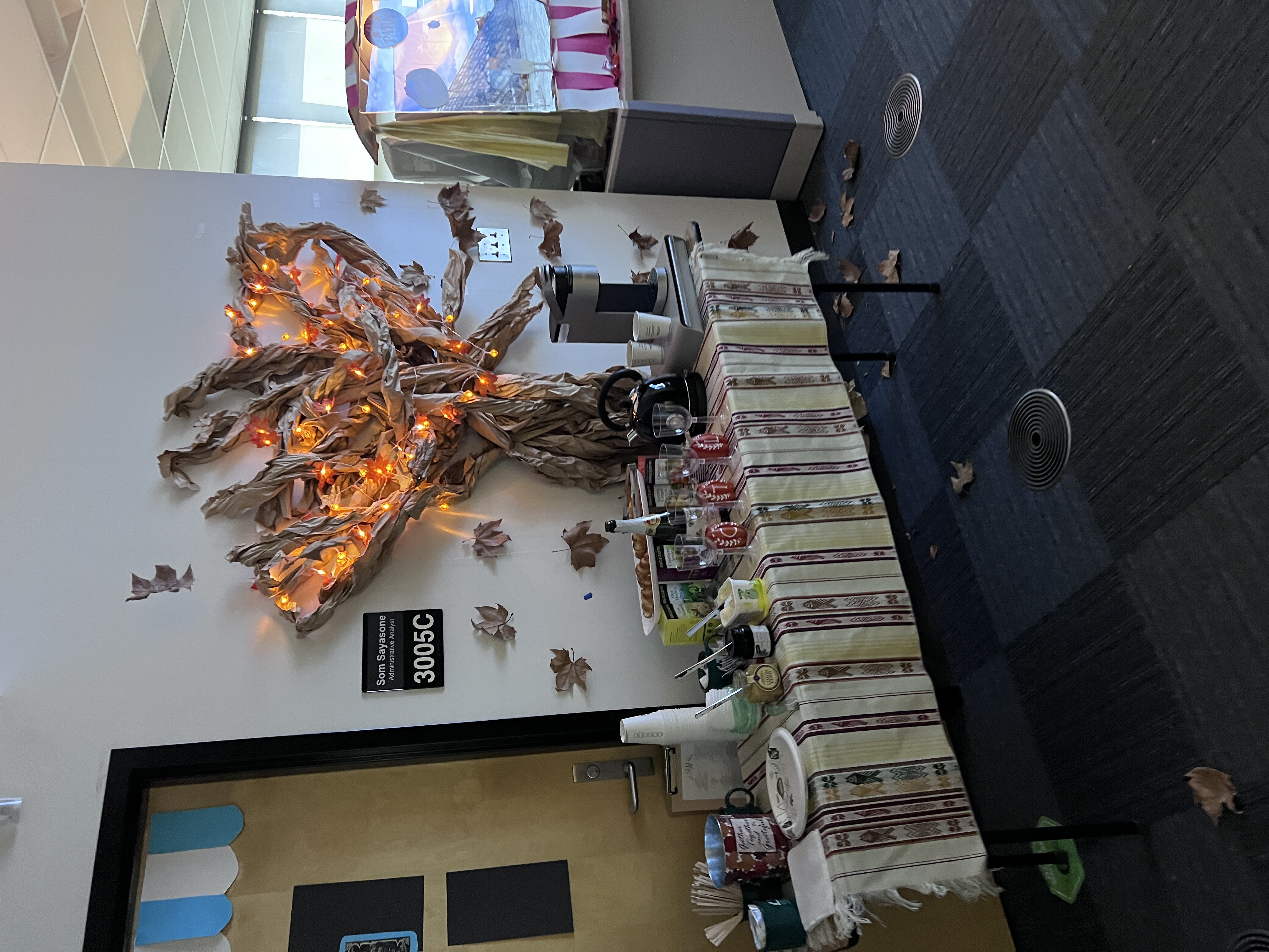 Center for Teaching and Learning “Fall in Paris”  coffee buffet in front of a paper tree with orange lights and leaves falling next to a bakery window display