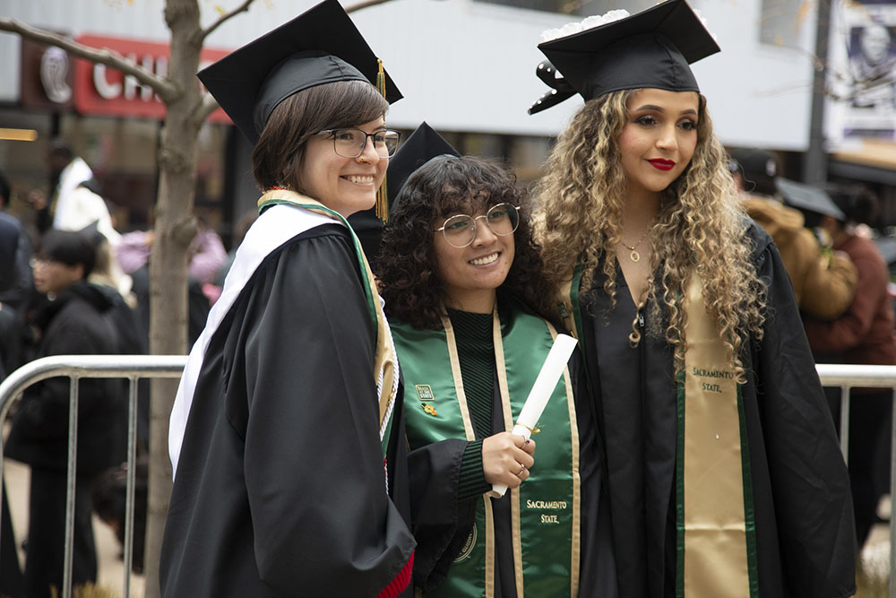three female students with their cap and gowns smiling at the camera