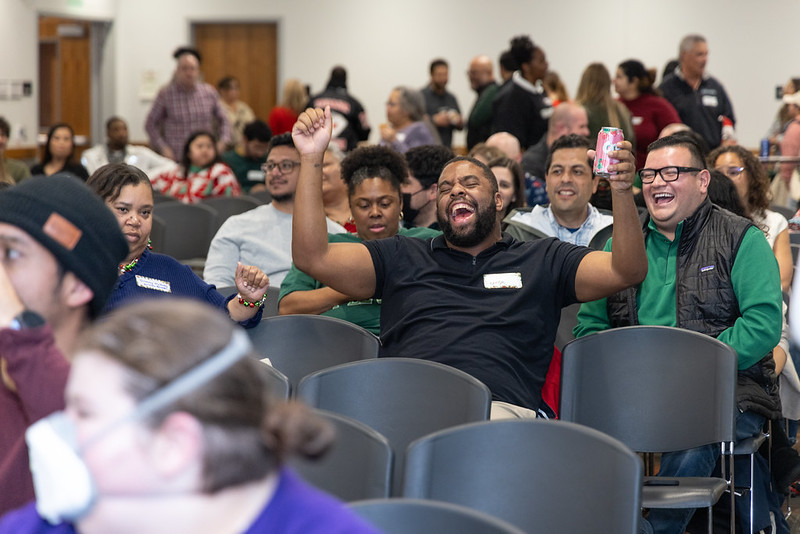 Staff sitting down and celebrating with his hand up while other staff smile