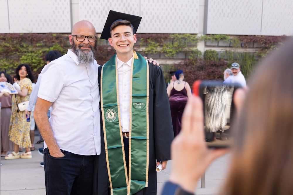 A parent and student in graduation gown smiling at the camera.