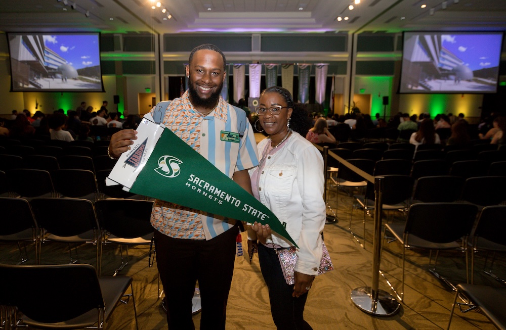 Man and woman smiling at the camera at an indoor event with green and gold lighting.
