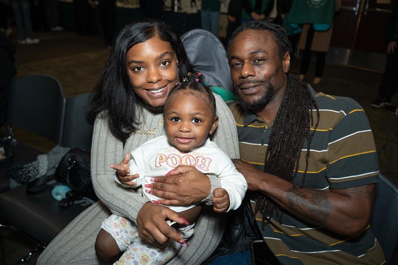 Student parents holding a baby and smiling at the camera
