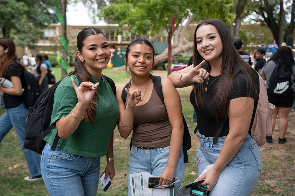 Three female students smiling at the camera with the stingers up gesture.