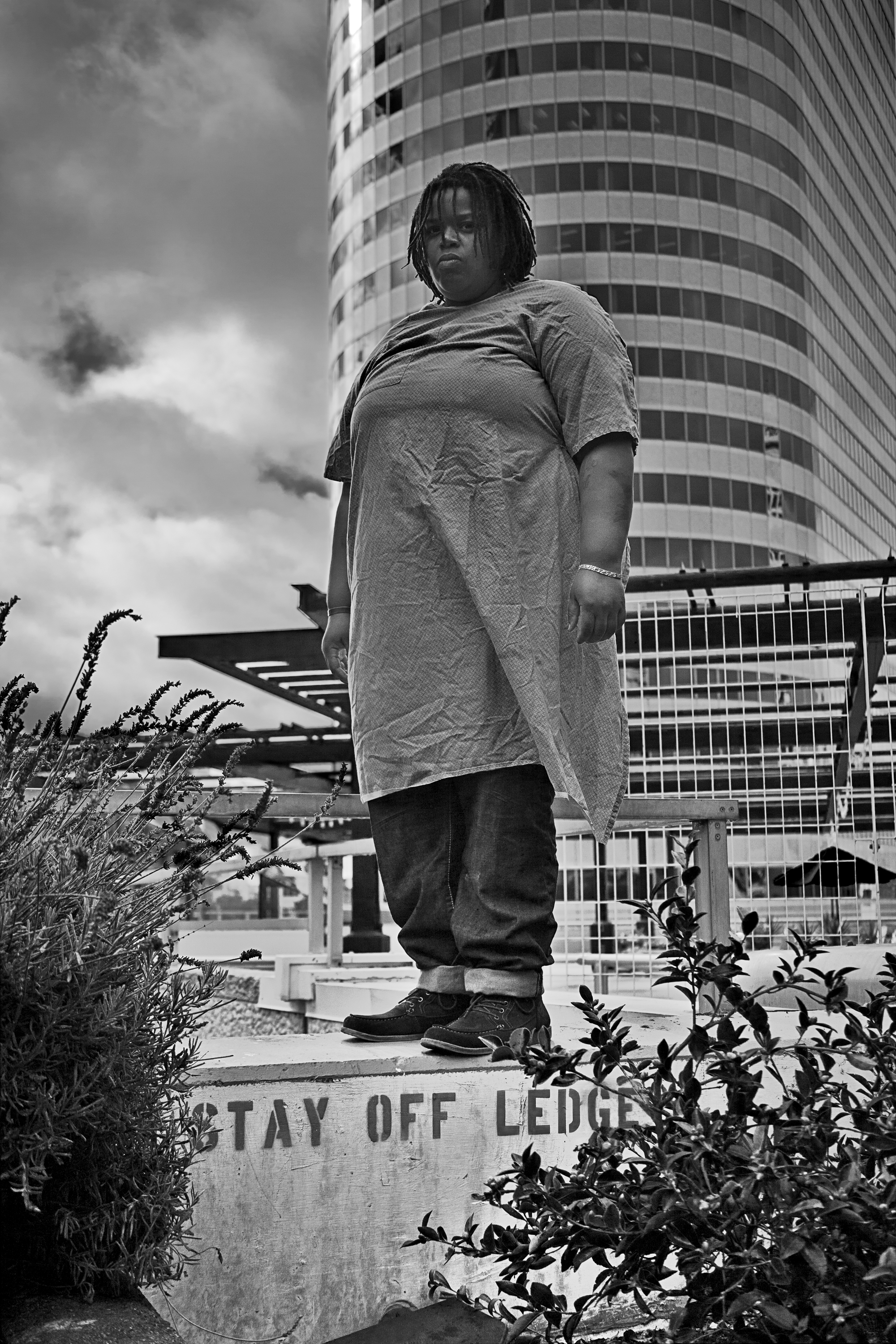 black and white photograph of a woman wearing a hospital gown standing on a ledge