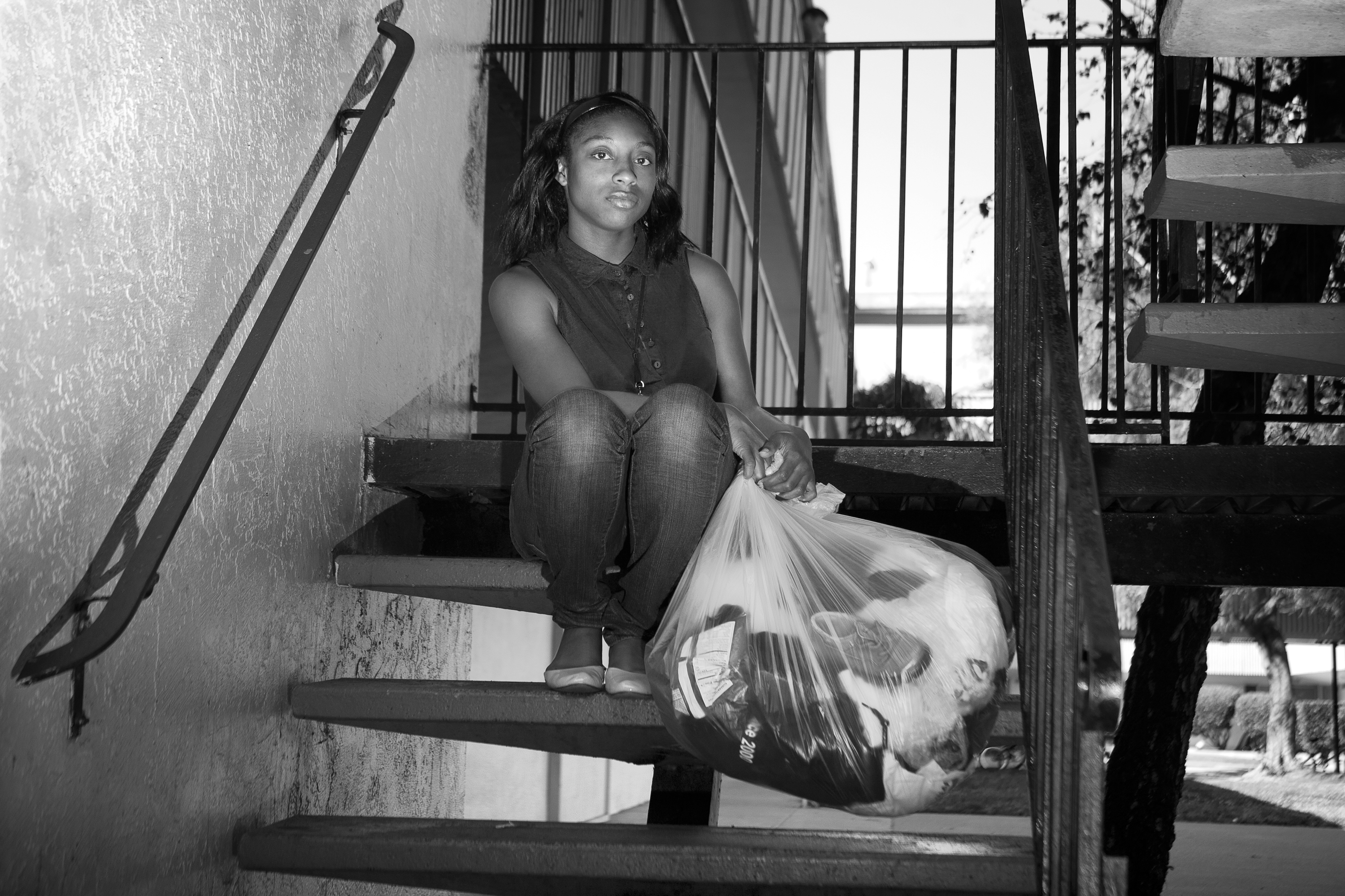 photograph of person sitting on stairs and holding a plastic bag of clothes